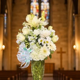 White floral arrangement in a clear glass vase with a ribbon bow