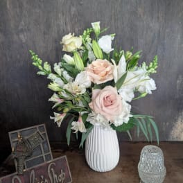 Blush roses and white lilies arranged in a white vase