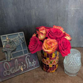 Red and yellow roses in a mosaic glass vase beside decorative plaques