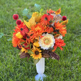 Orange and yellow floral arrangement in a white vase on grass