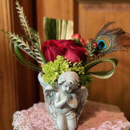 Red roses and green blooms in an angel vase with looped foliage and a peacock feather accent.