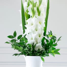 White gladiolus arrangement in a white vase with green foliage