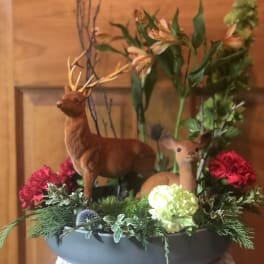 Floral arrangement with deer figurines in a low gray container