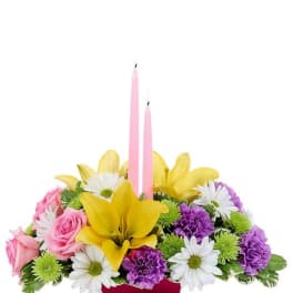 Pink candles in a mixed flower centerpiece with yellow lilies and daisies
