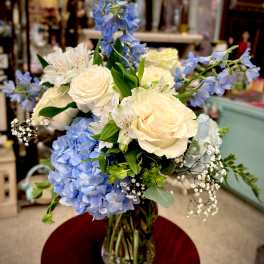 Bouquet of cream roses, blue hydrangeas, and white flowers in a glass vase