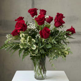 Red roses arranged in a clear glass vase with mixed greenery