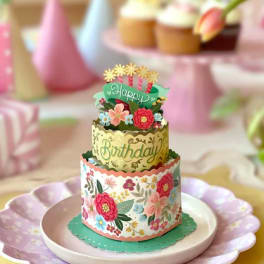 Tiered birthday cake with floral decorations and pastel party accents