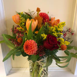 Mixed bouquet of orange tulips, red roses, and a peach dahlia in a glass jar