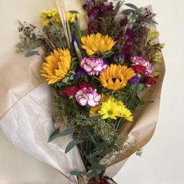 Bouquet of yellow sunflowers, pink carnations, and purple flowers wrapped in paper