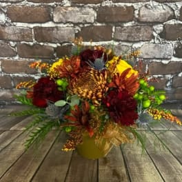 Autumn floral arrangement in a gold vase with burgundy and orange blooms