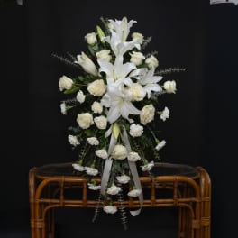 White lilies and roses arranged in a tall standing spray with ribbon