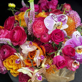 Bright mixed bouquet of pink roses, orchids, and orange blooms in brown wrap