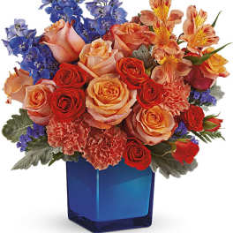 Bouquet of roses, carnations, and blue flowers in a blue glass vase