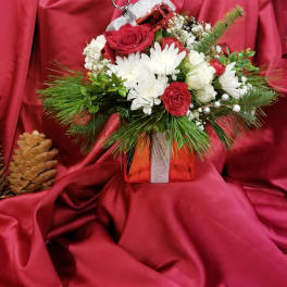 Holiday floral arrangement in a red gift box with a small ornament