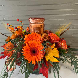 Orange floral arrangement with a pumpkin spice candle in a glass jar