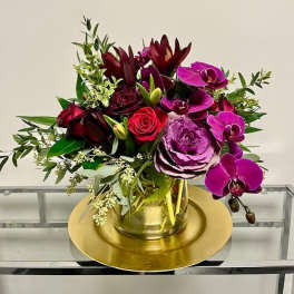 Bouquet of purple orchids, roses, and dark red blooms in a glass vase