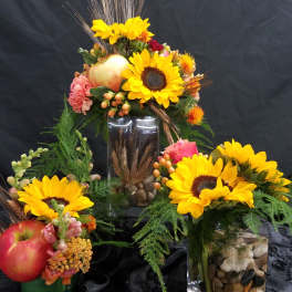 Sunflower arrangements in glass vases with apples and decorative grasses