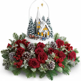Christmas floral arrangement with red roses, pinecones, and a snowy church ornament