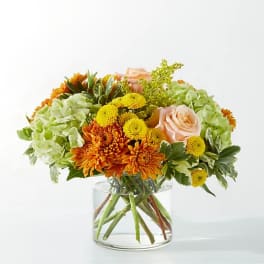 Bouquet of orange and yellow flowers with pale pink roses in a clear glass vase
