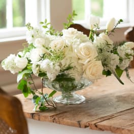White roses and white blooms arranged in a clear glass compote vase
