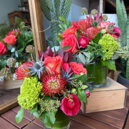 Bright mixed bouquet in a green glass vase with coral, pink, and lime blooms
