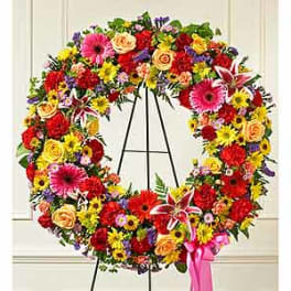 Colorful floral wreath on a black stand with a pink ribbon