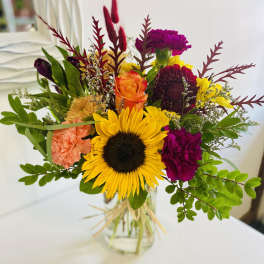 Bright mixed bouquet with a sunflower, roses, and carnations in a glass vase