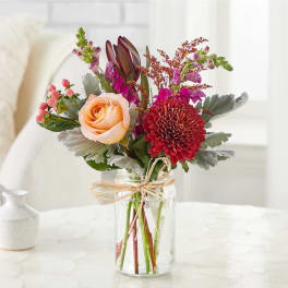 Mixed bouquet of peach and red flowers in a clear glass jar vase