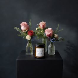 Three small rose arrangements in glass vases with a candle in front