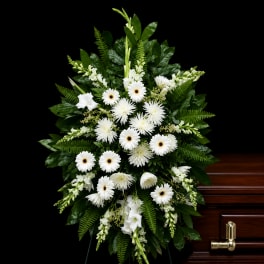 White funeral spray with daisies and lilies on a dark wood casket