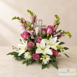Pink roses and white lilies arranged around a clear glass cross