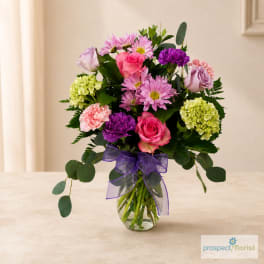 Mixed pink and purple bouquet in a glass vase with a purple ribbon