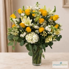 Yellow roses and white lilies arranged in a clear glass vase