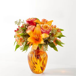 Orange and pink mixed bouquet in an amber glass vase