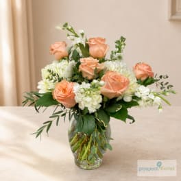 Peach roses and white flowers arranged in a clear glass vase