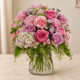 Pink and lavender roses with small purple daisies in a glass vase