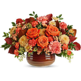 Orange roses and mixed fall flowers in a brown glass vase