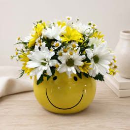Yellow smiley-face vase filled with white and yellow daisies
