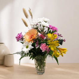 Mixed bouquet of daisies, lilies, and pink flowers in a clear glass vase