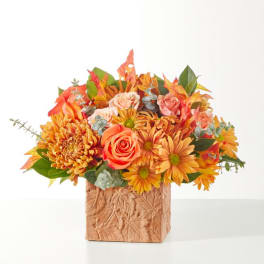Autumn bouquet of orange and pink flowers in a textured square vase