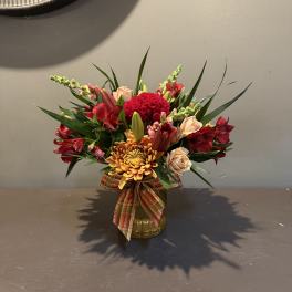 Mixed bouquet of red, peach, and yellow flowers in a glass vase with a plaid ribbon