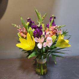 Mixed bouquet of yellow lilies, pink alstroemeria, and purple stock in a glass vase