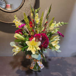 Mixed bouquet with yellow lilies, red and magenta blooms in a glass vase