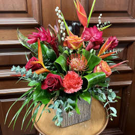 Tropical bouquet with red roses, orange bird of paradise, and pink blooms in a wooden vase