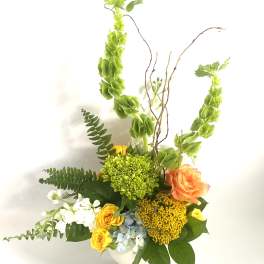 Tall mixed flower arrangement in a white vase with orange and yellow blooms