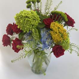 Mixed bouquet of red roses, blue hydrangea, and green chrysanthemums in a glass vase