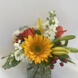 Mixed bouquet with a sunflower, lilies, roses, and white blooms in a glass vase