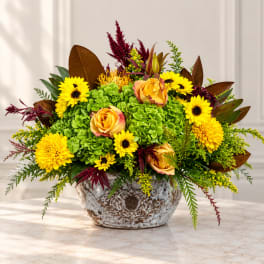 Yellow flowers and orange roses arranged in a rustic ceramic bowl