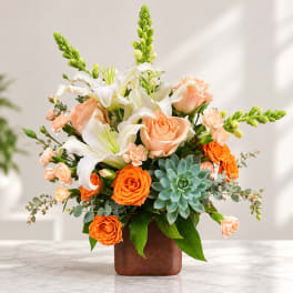 Peach roses and white lilies in a brown vase with a succulent accent