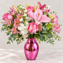 Pink lilies, roses, and white blooms in a shiny pink vase